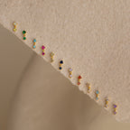Emerald Drop Studs featuring vibrant gemstones set in a diagonal line, displayed on a beige textured surface.