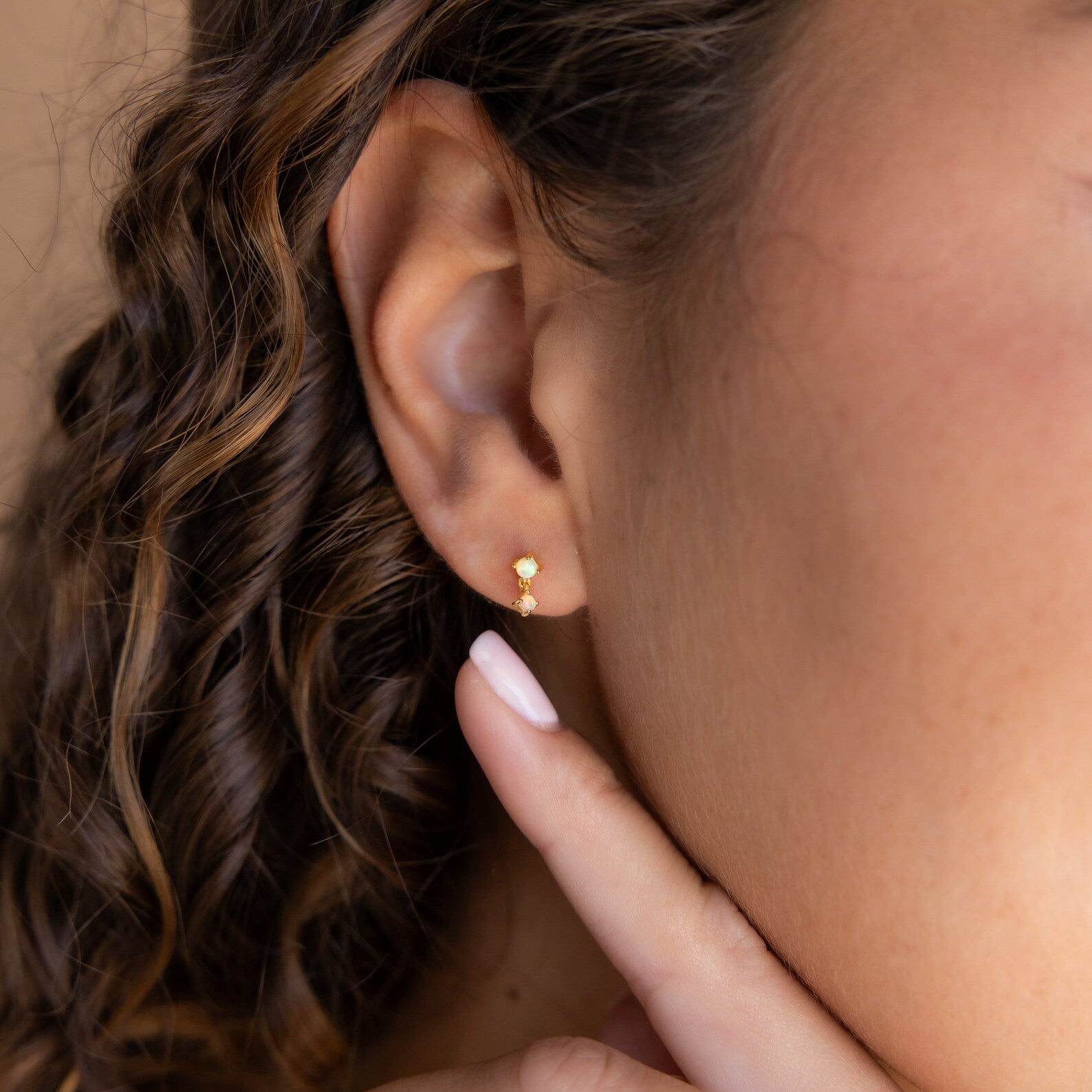 A close-up of a woman's ear wearing Amethyst Drop Studs, with her fingers gently touching her chin.