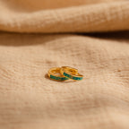 Two delicate Green Opal Inlay Huggies rest on beige textured fabric, offering a subtle pop of color to elevate your everyday style.