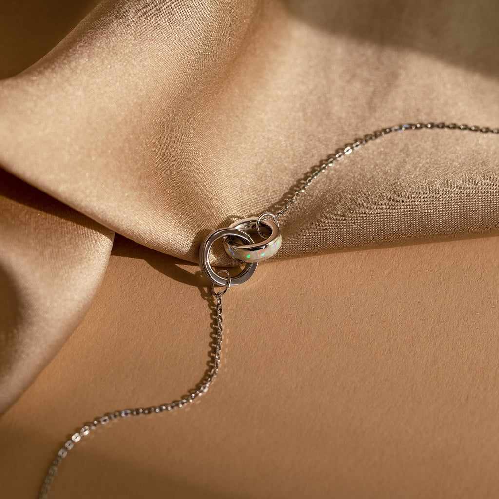 Interlocking Opal Inlay Bracelet displayed on beige satin fabric, ideal for stacking with a silver chain necklace or pairing with other minimalist jewelry pieces.