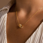 Gold interlocking opal inlay necklace with two linked circle pendants on a delicate chain, styled with a pleated ivory blouse.
