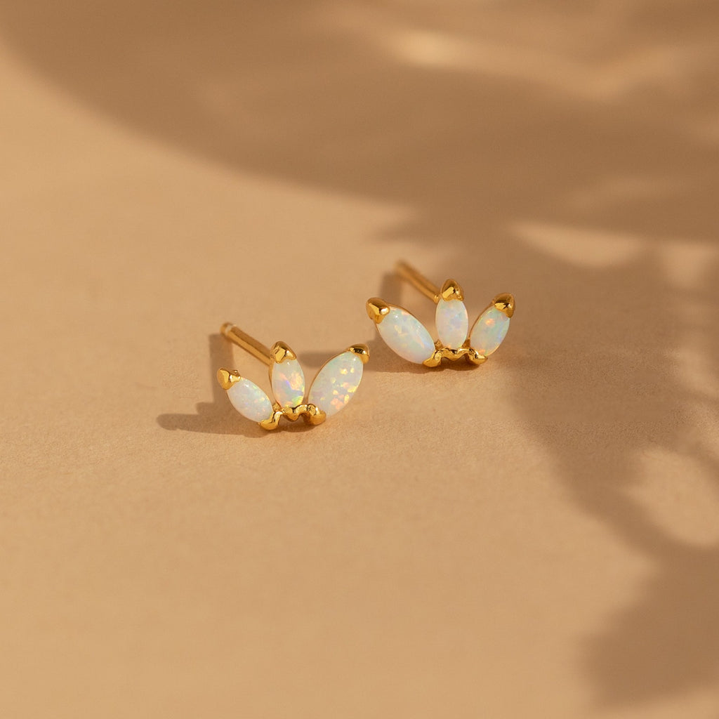 Opal Marquise Studs feature three marquise-shaped opal stones arranged in a delicate floral design, showcased on a neutral beige background.