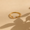 The Marquise Opal Diamond Ring features a gold band with a marquise opal center stone and two small diamonds on each side, displayed on a beige textured surface.