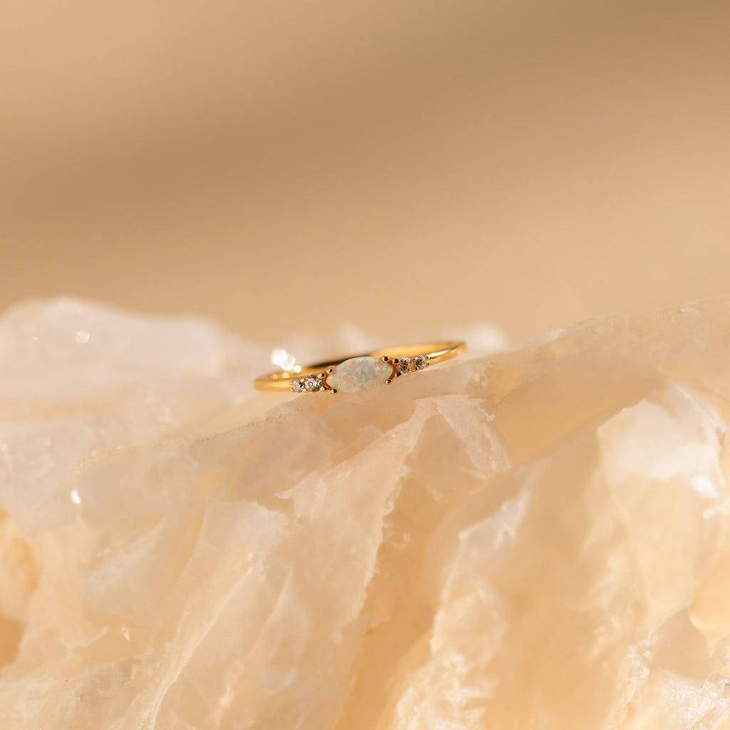 The Marquise Opal Diamond Ring features a central marquise opal accented by two diamonds, elegantly showcased on a light, translucent crystal.
