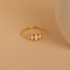 The Marquise Opal Statement Ring features four irregular white stones set in gold, radiating vintage charm, and is displayed on a beige surface next to a round white object.