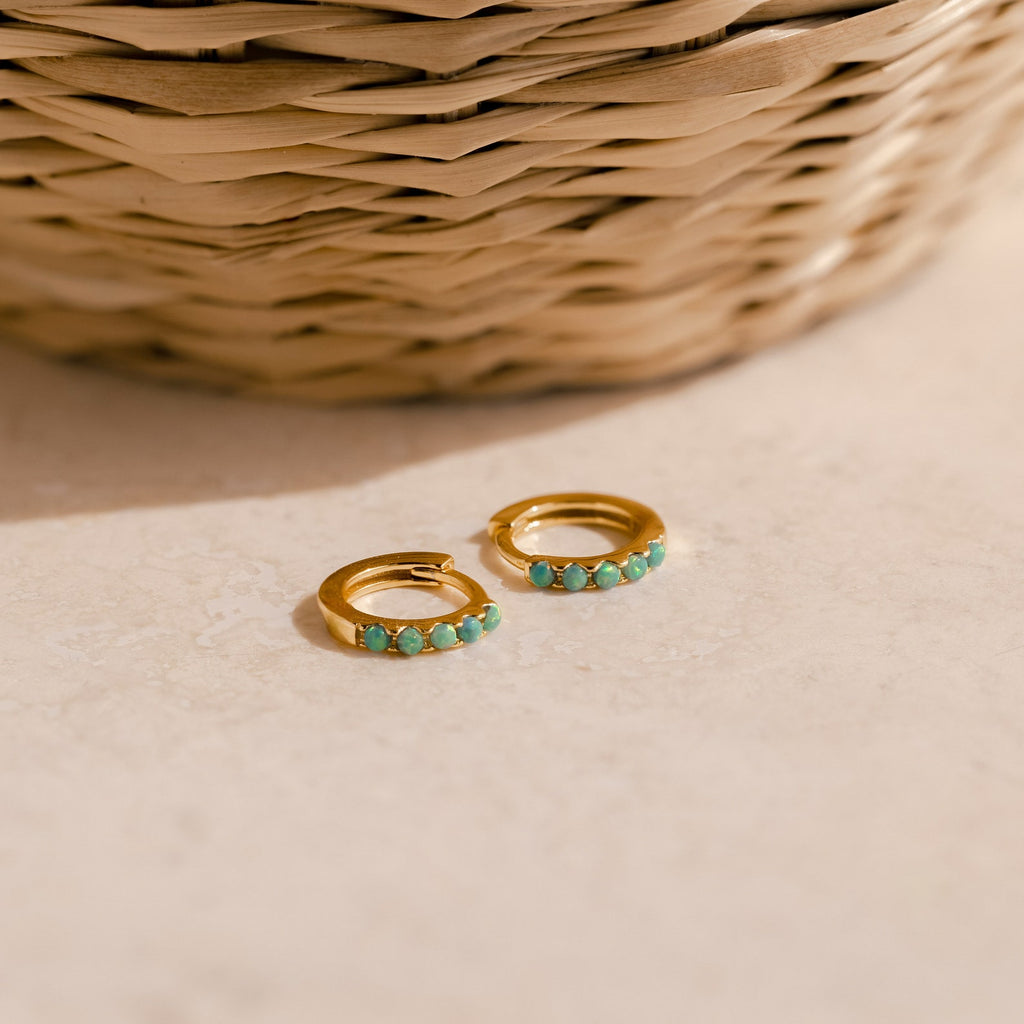 Garden Green Opal Huggies rest on a beige surface, ideal for stacking. A woven basket adds a natural touch in the background.