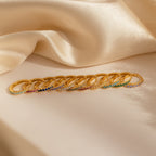 A row of gold rings, including Vera Pave Ruby Huggies with vibrant gemstones, displayed on beige satin fabric.