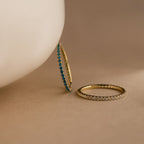 Two Eternity Birthstone Rings—one with blue gemstones, one with clear—rest on a beige surface. These customizable rings make a thoughtful Christmas gift.