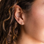 Close-up of a woman's ear with an Amethyst Drop Stud—one of our elegant birthstone earrings—nestled amid curly brown hair framing her face.