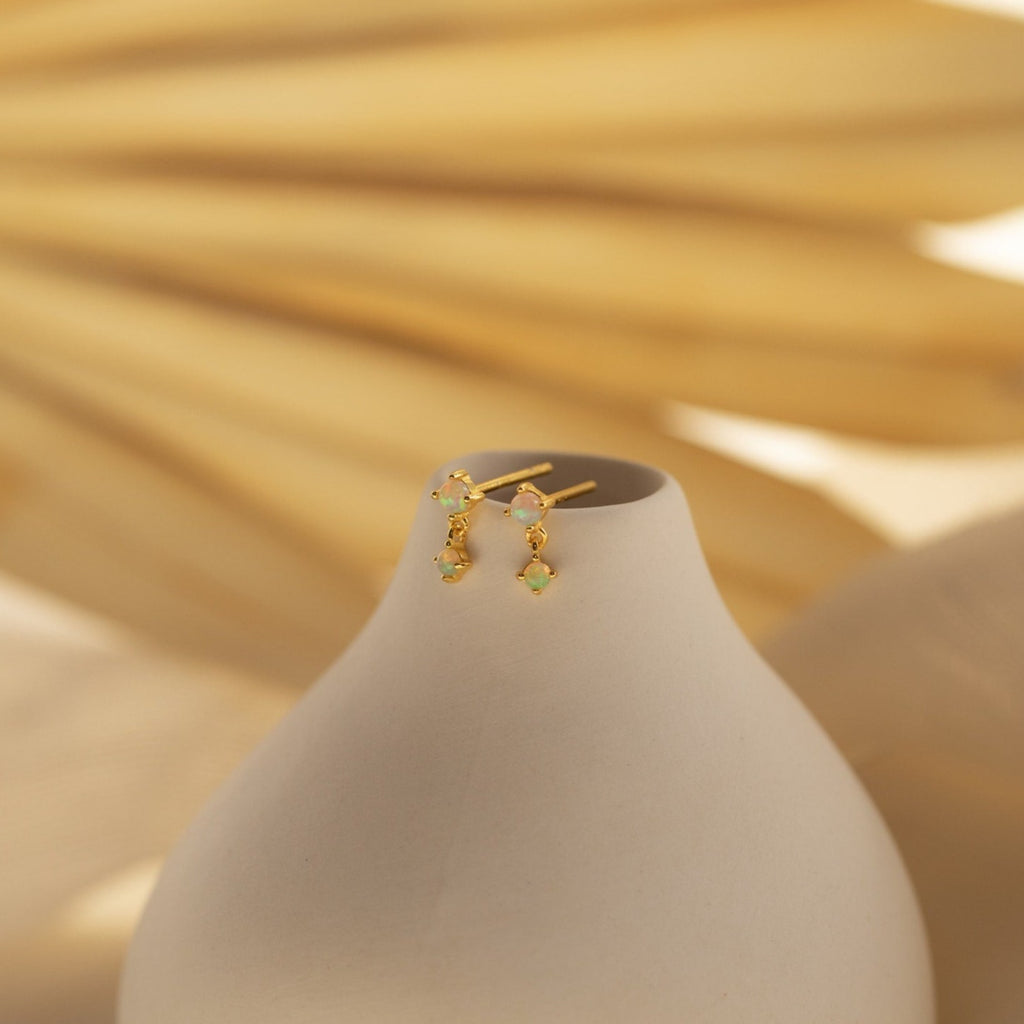 Opal Drop Studs accessorize a smooth white vase, set against a soft beige background.