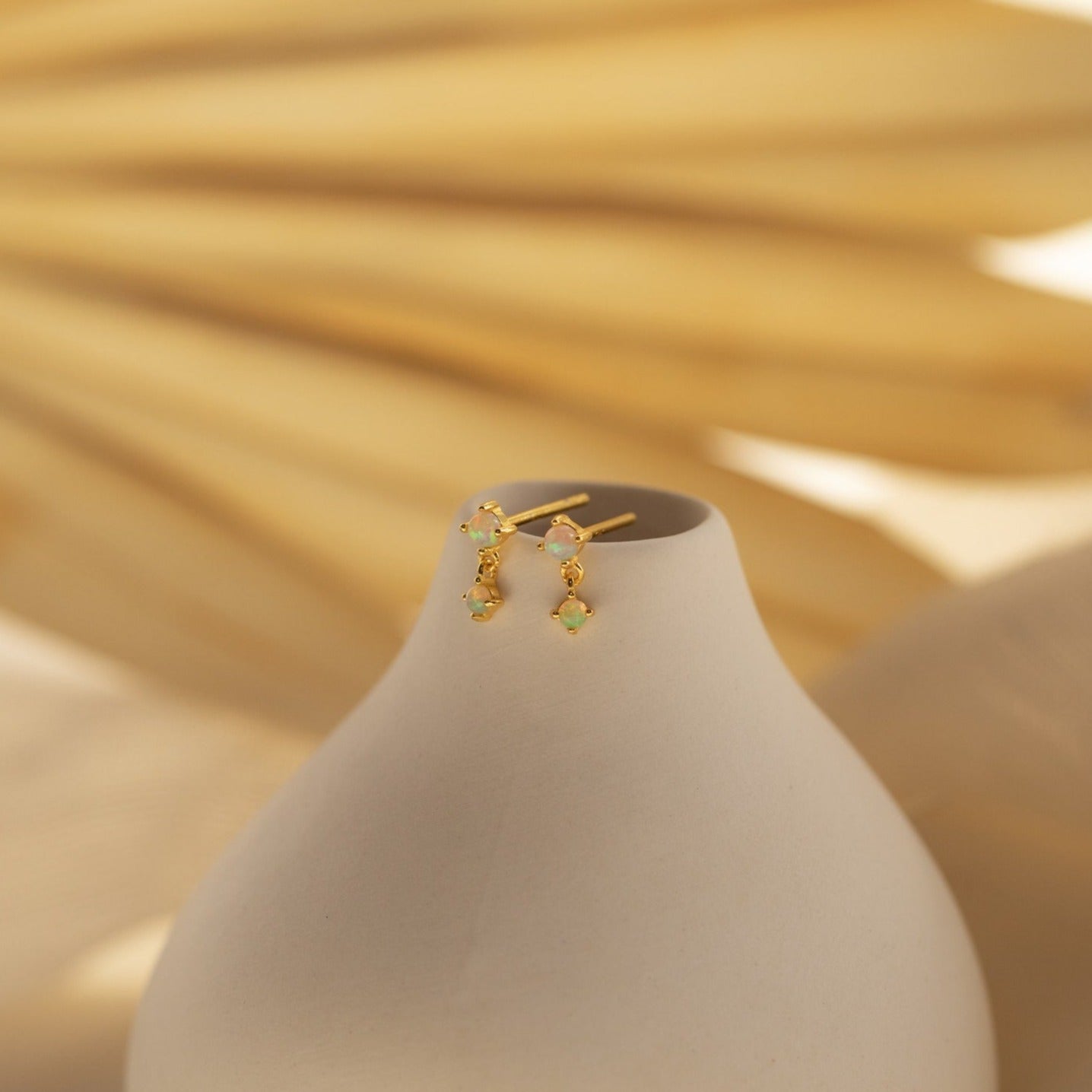 Opal Drop Studs accessorize a smooth white vase, set against a soft beige background.