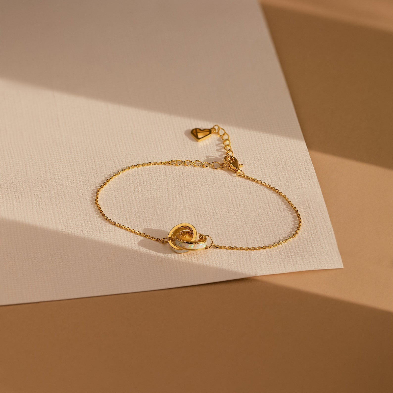 The Interlocking Opal Inlay Bracelet features a delicate design, ideal for minimalist jewelry lovers. Shown on textured white and beige paper in natural light.
