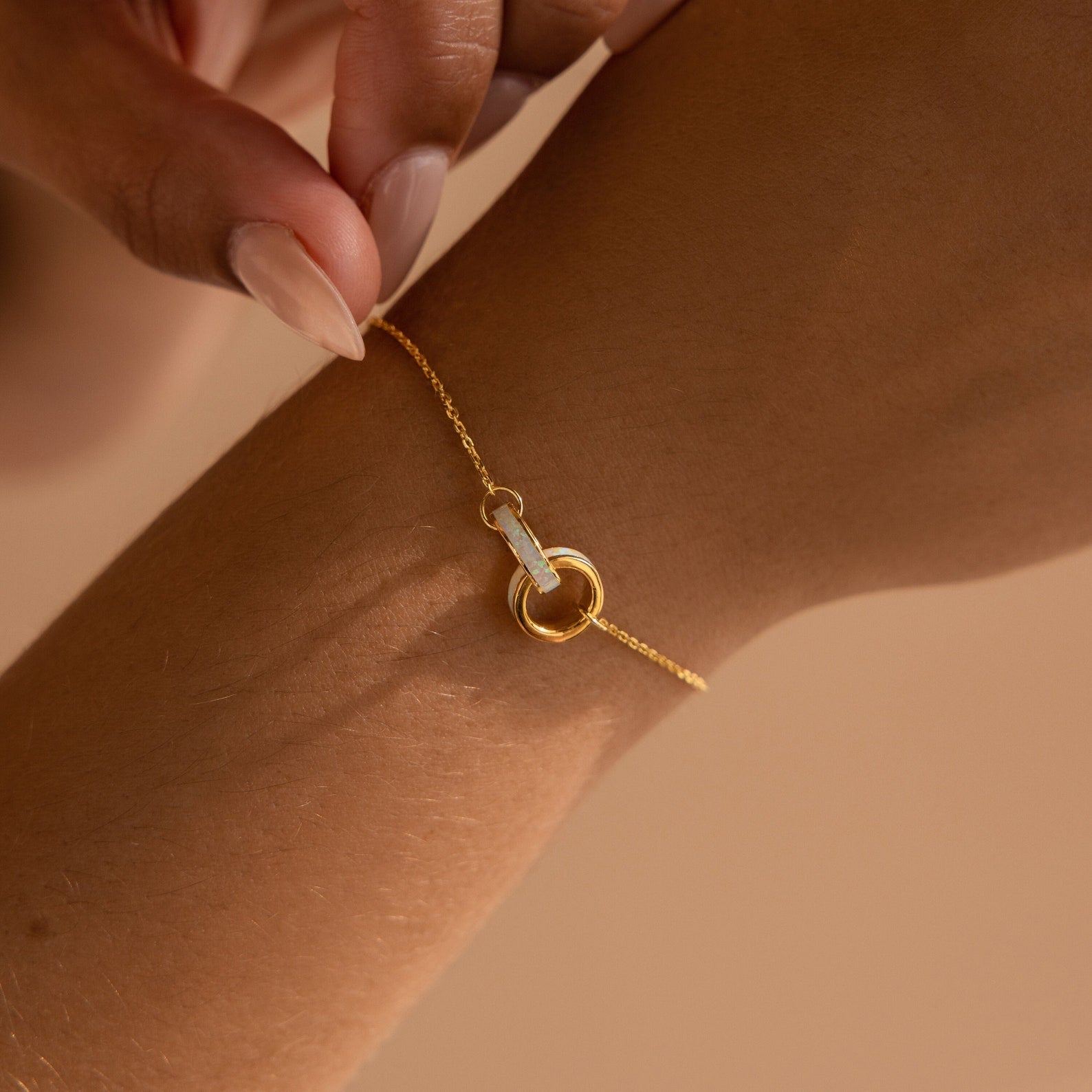 The Interlocking Opal Inlay Bracelet features a gold chain with opal-inlaid circles and bar details, inspired by minimalist jewelry style, worn on the wrist as a hand adjusts its clasp.