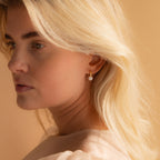  three-quarter portrait of a blonde woman wearing a single gold Pearl Drop Huggie, her gaze directed softly to the side.