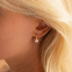  close-up side profile of a woman with blonde hair wearing a gold Pearl Drop Huggie on her earlobe.
