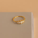 The Marquise Opal Statement Ring features five white opals, shown on a closed beige book against a soft beige background, radiating vintage allure and classic style.