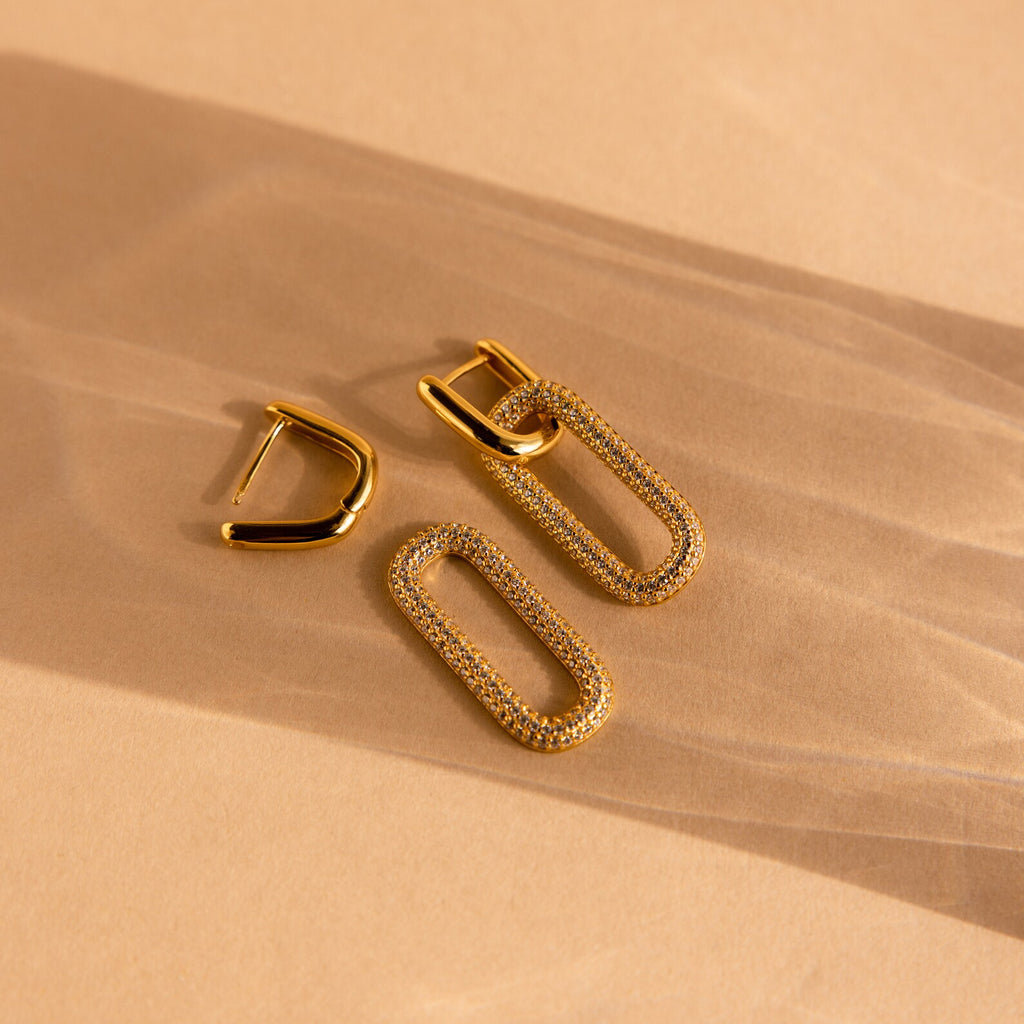 Pave Link Hoops: Gold hoops with diamond-accented rectangular loops offer a refined look, shown on a beige background with soft shadows—an elegant jewelry choice.