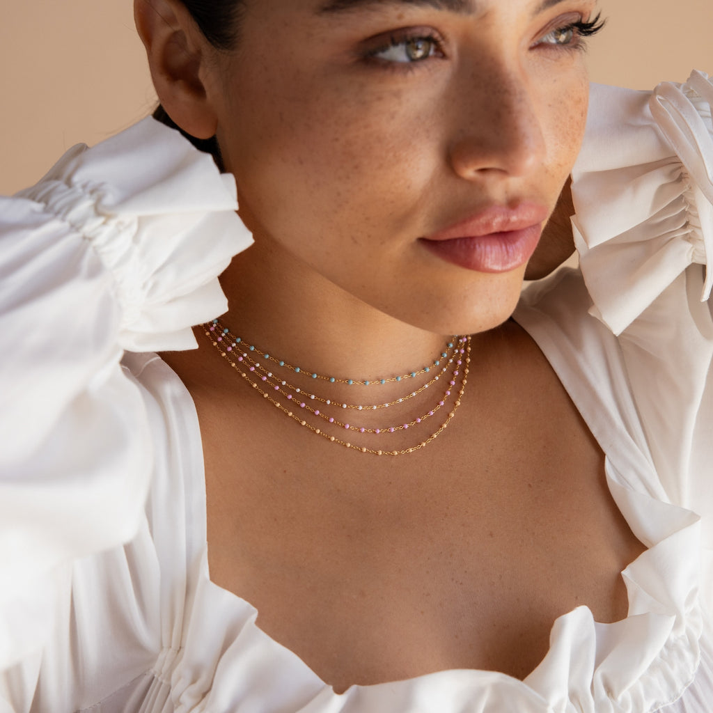 Woman in a white ruffled top with a beachy vibe, wearing the Peach Station Necklace adorned with colorful beads, looking off to the side.