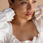 Woman in a white ruffled top with a beachy vibe, wearing the Peach Station Necklace adorned with colorful beads, looking off to the side.