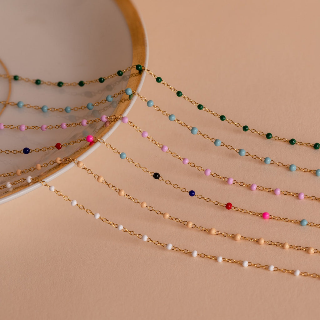 Beaded Station Necklaces with delicate gold chains and colorful beads are arranged on a plate against a beige background, offering playful jewelry that adds a trendy touch to any outfit.