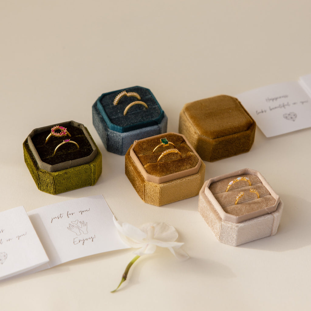 Five Velvet Ring Box products, featuring a 3-slot option, showcase gold rings beside handwritten cards and a white flower on a cream surface.