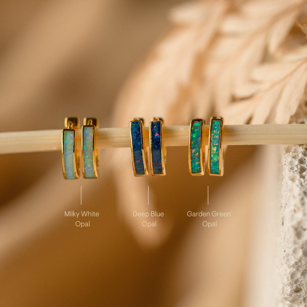 Three pairs of Opal Inlay Earrings—milky white, deep blue, and garden green from our Opal Collection—are beautifully displayed on a stick.