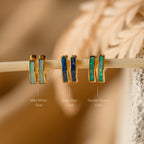 Three pairs of Opal Inlay Earrings—milky white, deep blue, and garden green from our Opal Collection—are beautifully displayed on a stick.
