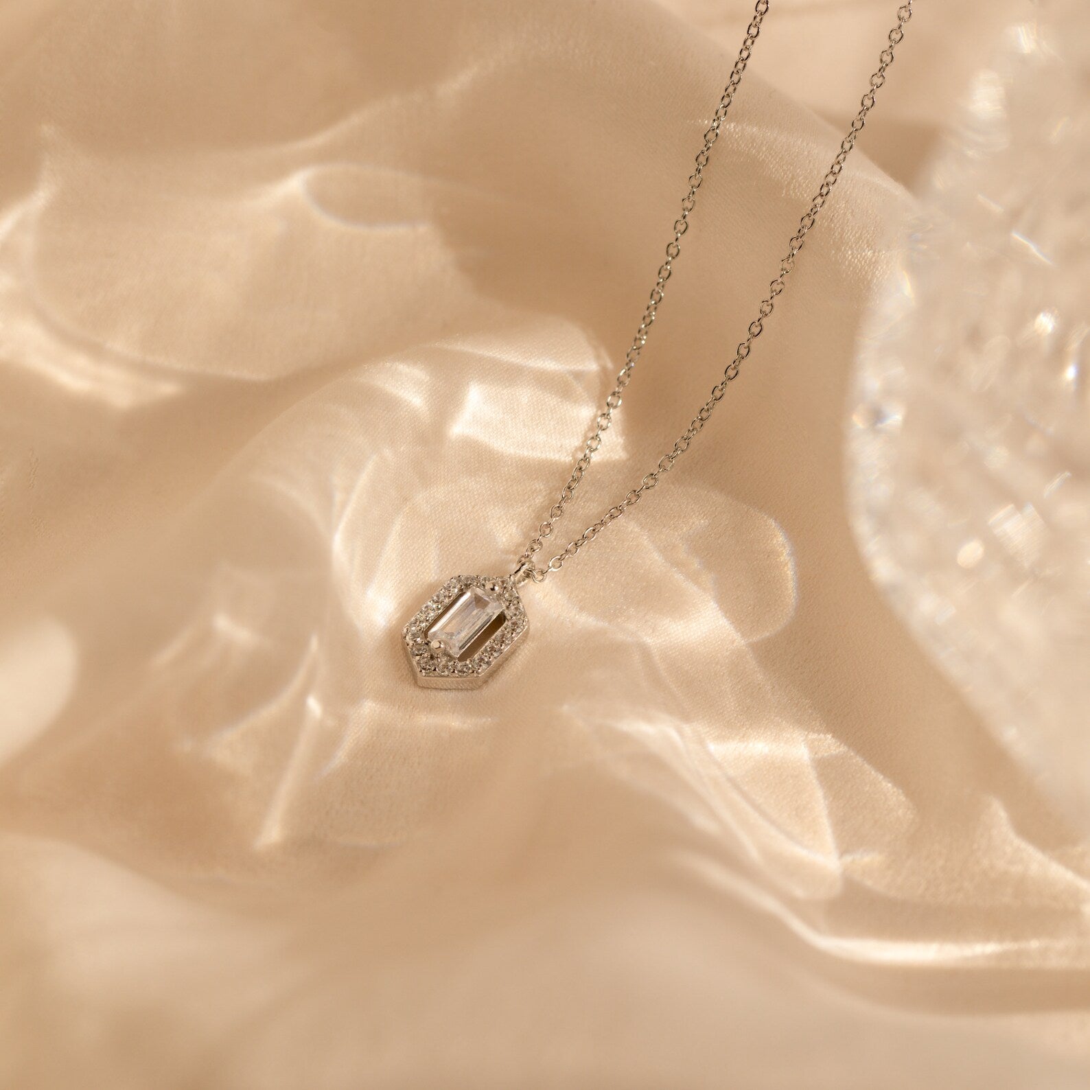 The Daydreamer Diamond Necklace exudes timeless elegance as it rests on soft ivory satin, with gentle light reflections highlighting this luxurious diamond accessory.