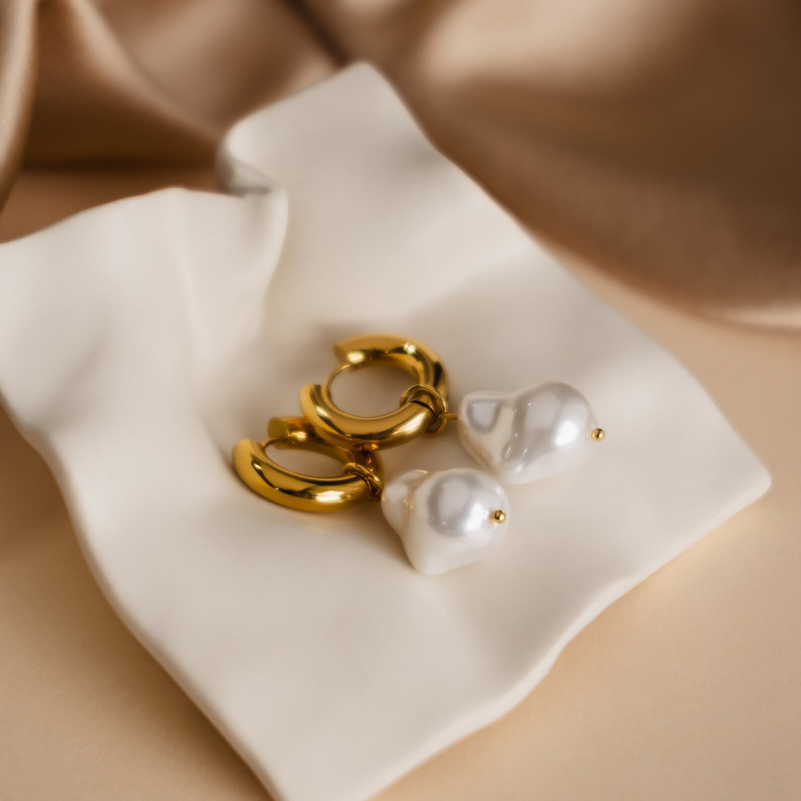 Baroque Pearl Drop Hoops—gold hoops featuring large white pearls on a soft cream fabric background—make stunning statement earrings or elegant wedding jewelry.