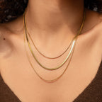 Close-up of a person wearing the Triple Layered Chain Necklace, which features gold herringbone and snake chains, styled with a brown top.