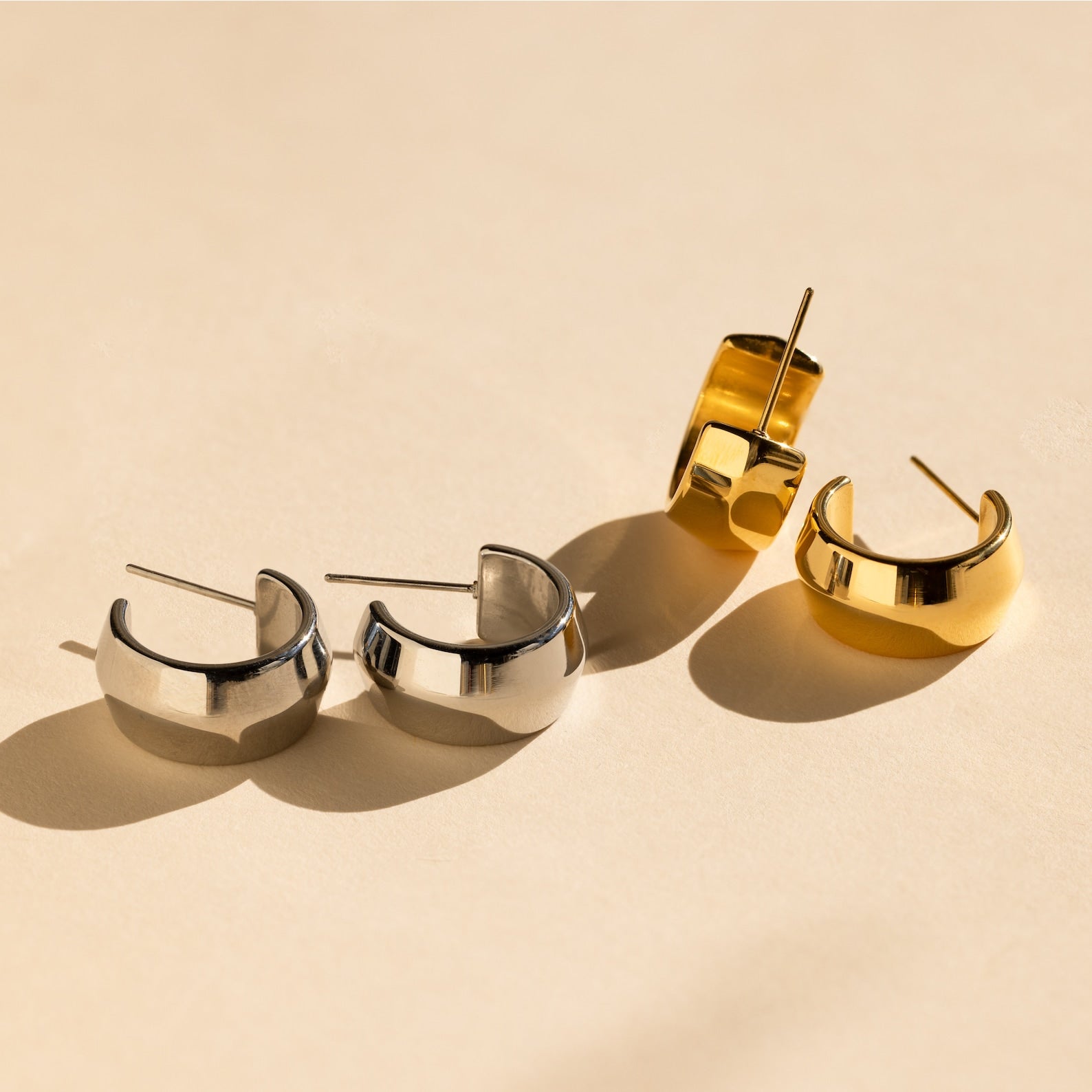 The Chunky Bold Hoops set features two pairs of statement earrings—one silver, one gold—that pop beautifully against a light beige background and add trendy flair to any look.