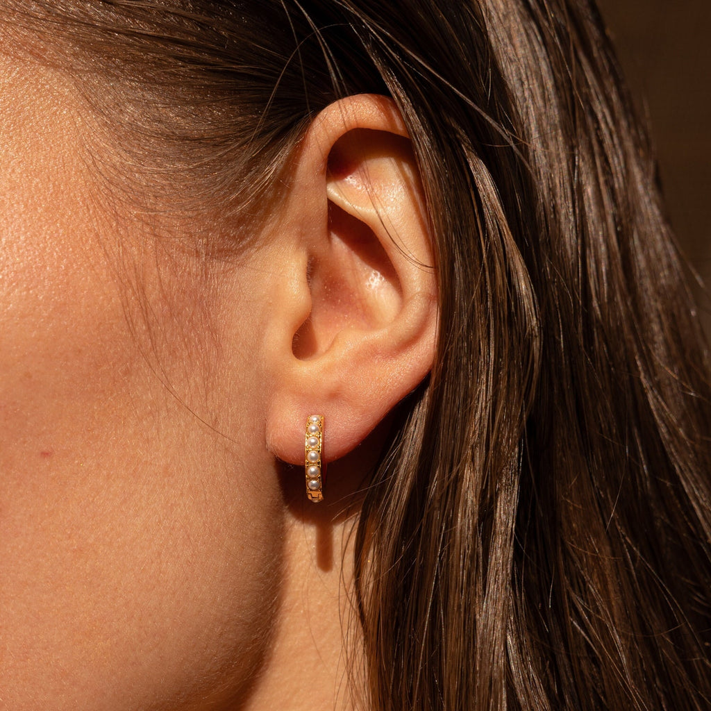 Gold pearl huggie earring worn on a model’s ear, shown close-up with natural lighting and wet-styled hair.