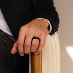 A person wearing a Classic Men's Black Rings Set rests their hand on a beige chair, highlighting understated men's jewelry.