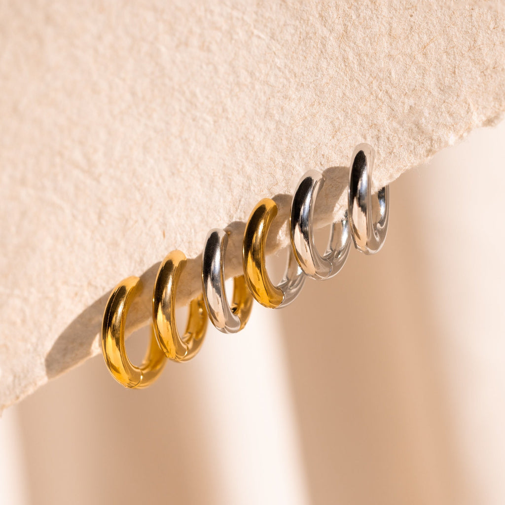 Six Chunky Hoops—three gold and three silver—are displayed on a textured beige surface.