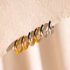 Six Chunky Hoops—three gold and three silver—are displayed on a textured beige surface.