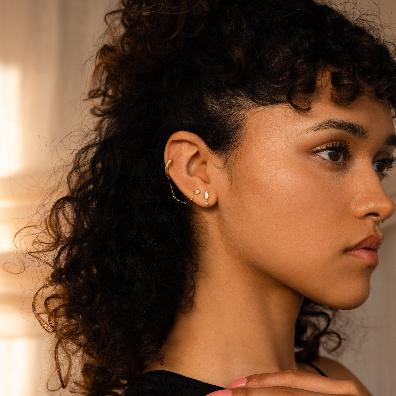 A woman with curly hair wears Art Deco Drop Studs, gazing to the side in warm lighting.