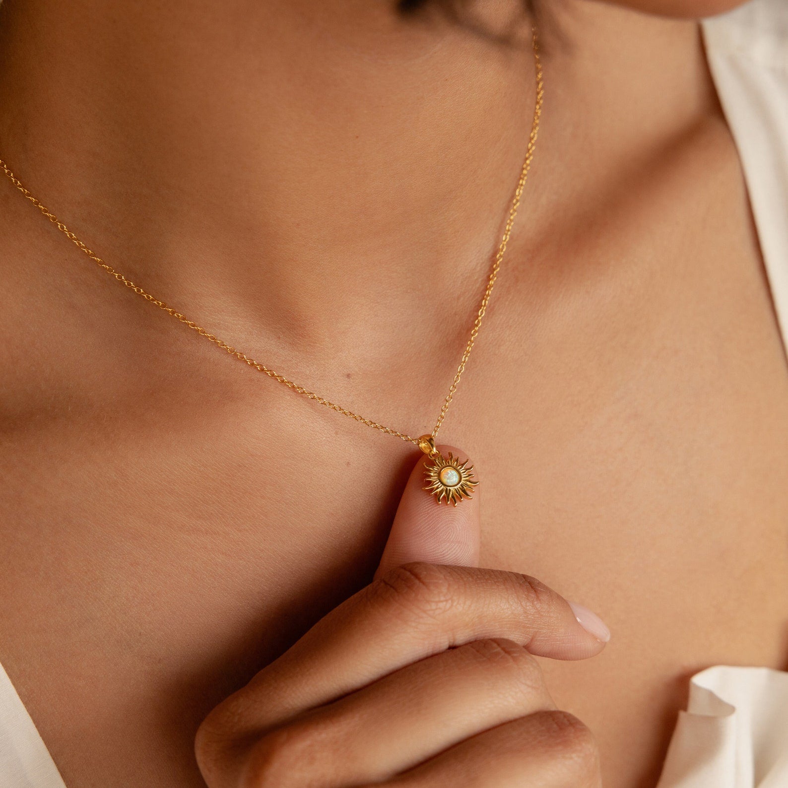 A person delicately holds the Opal Sun Necklace pendant to their chest, highlighting this elegant and charming jewelry piece.