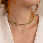 Close-up of a woman wearing two delicate layering necklaces—a green Emerald Tennis Choker Necklace and a white necklace—styled elegantly with a white top.