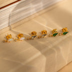 The Opal Kite Drop Earrings—gold with opal and geometric design—are displayed on beige fabric.