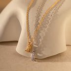 The Cowboy Boot Necklace comes in gold and silver with a western boot pendant, displayed on a curved beige surface—perfect for adding charm to your look.