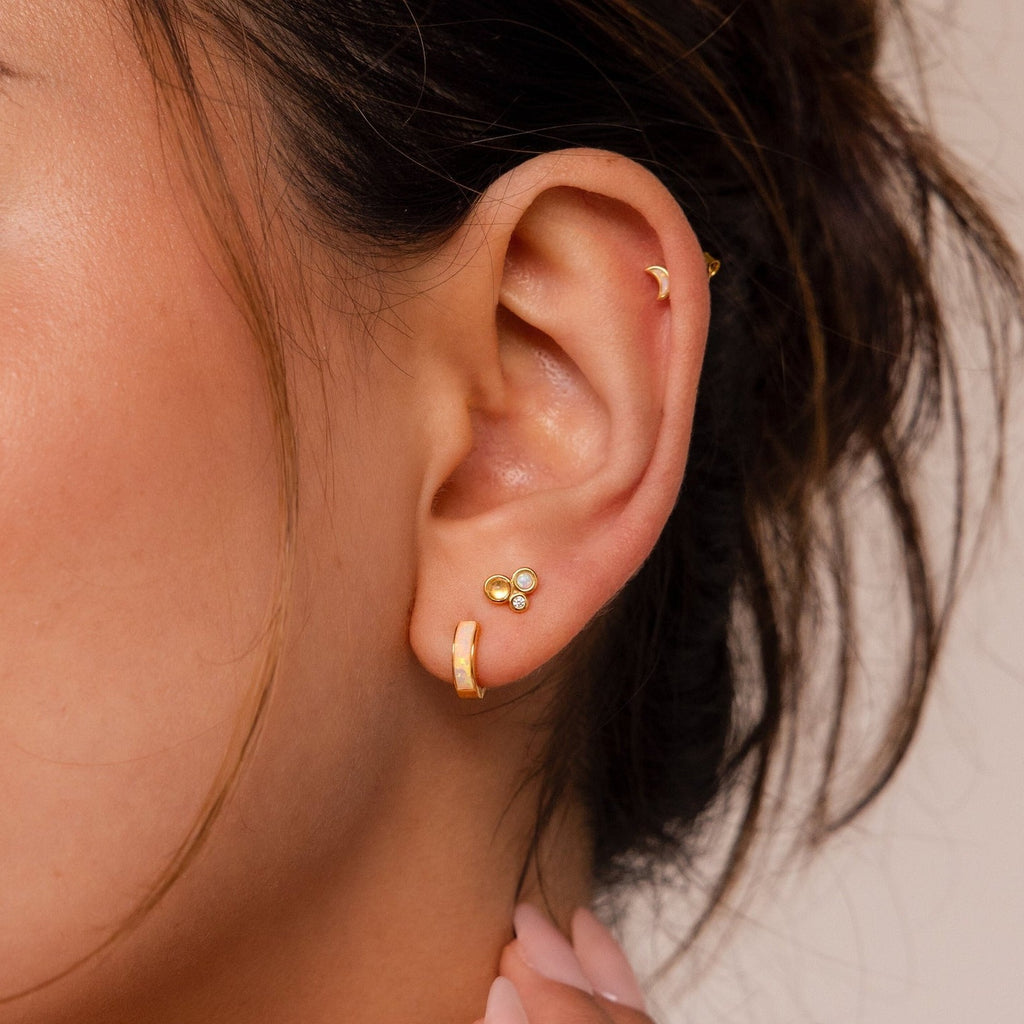 Close-up of a woman's ear adorned with the Opal Inlay Earrings Set: a gold hoop, a three-stone opal inlay stud, and a tiny crescent on the helix—an elegant jewelry set gift for her.