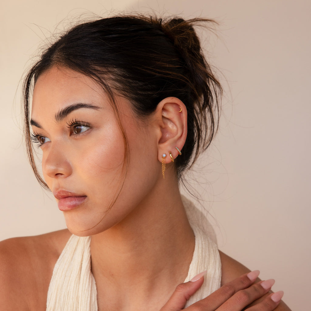 A woman with a scarf around her neck showcases her style, complemented by Opal Chain Earrings from her jewelry collection.