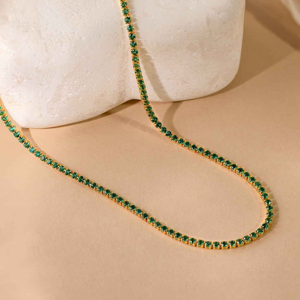 Gold tennis necklace with round green gemstones displayed against a neutral background.