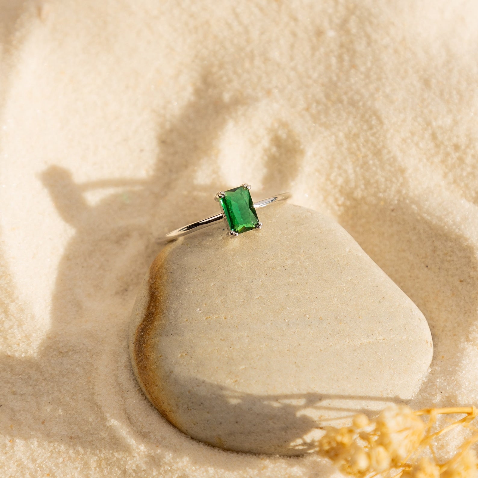 The Harley Emerald Ring - Silver features a rectangular green gemstone set in silver, resting on smooth stone and evoking classic Art Deco and vintage elegance.