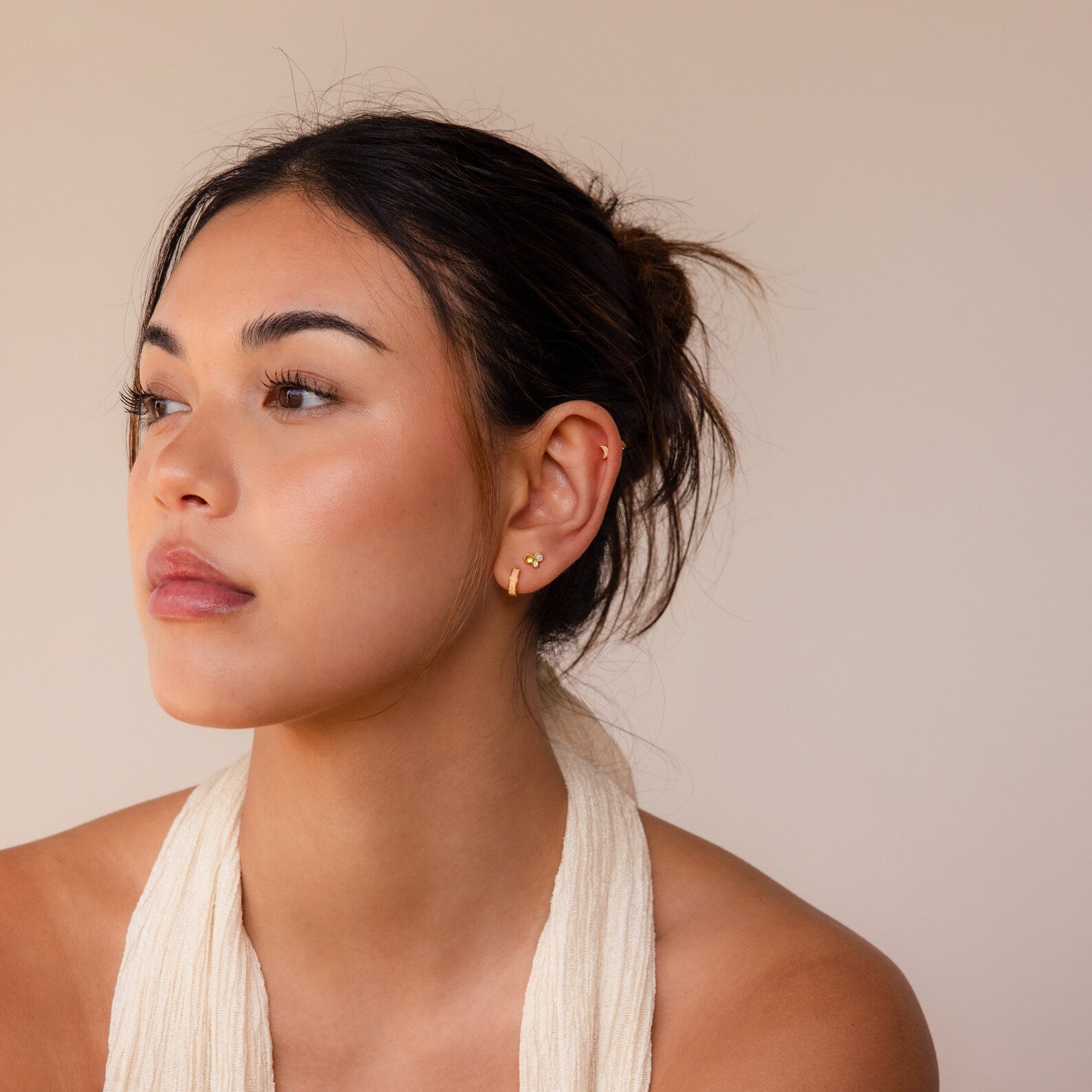 A woman with a neutral expression gazes left, wearing a cream halter top and the Opal Inlay Earrings Set against a beige background.