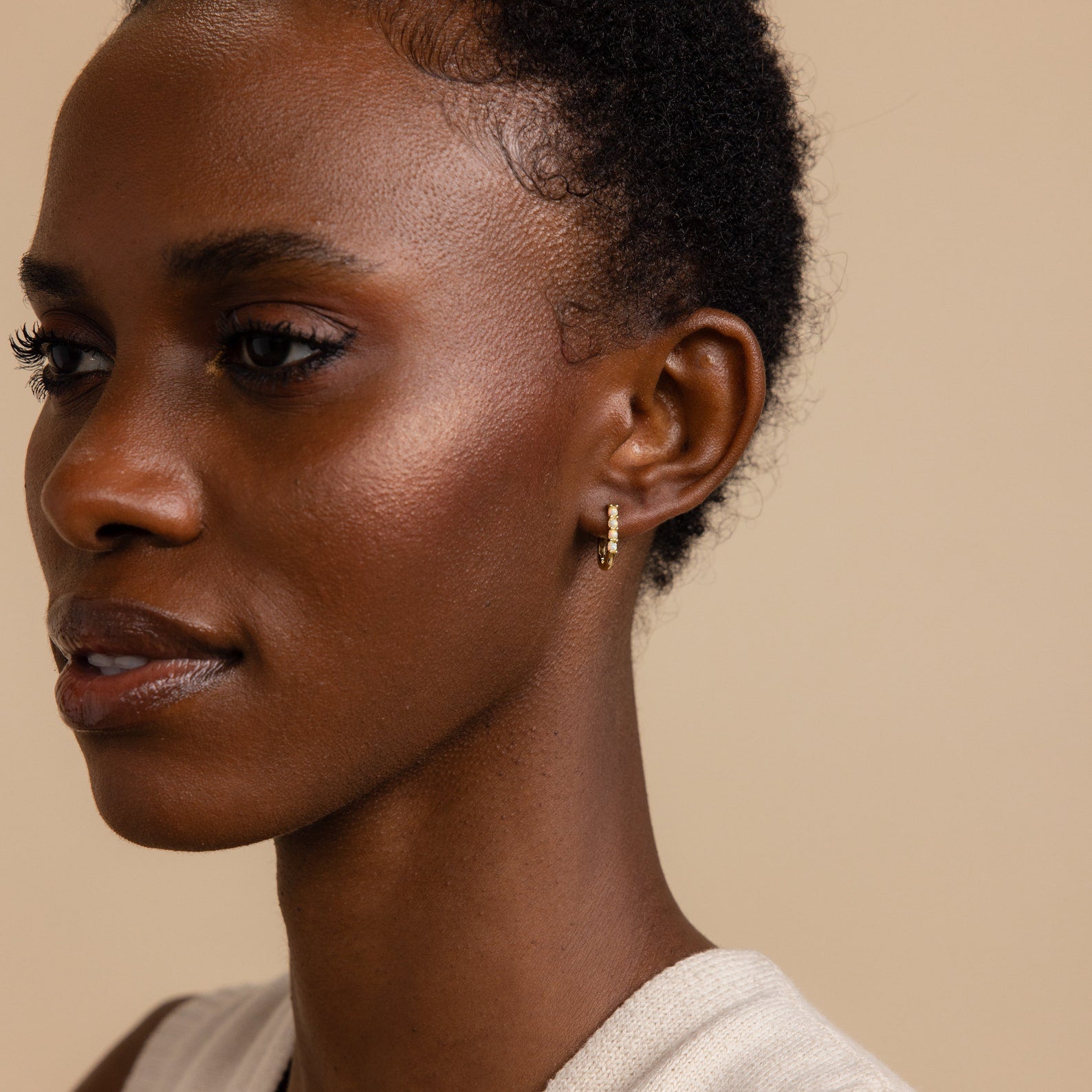 A woman with short curly hair wears the Opal Link Hoops and a sleeveless top, facing left against a beige background.