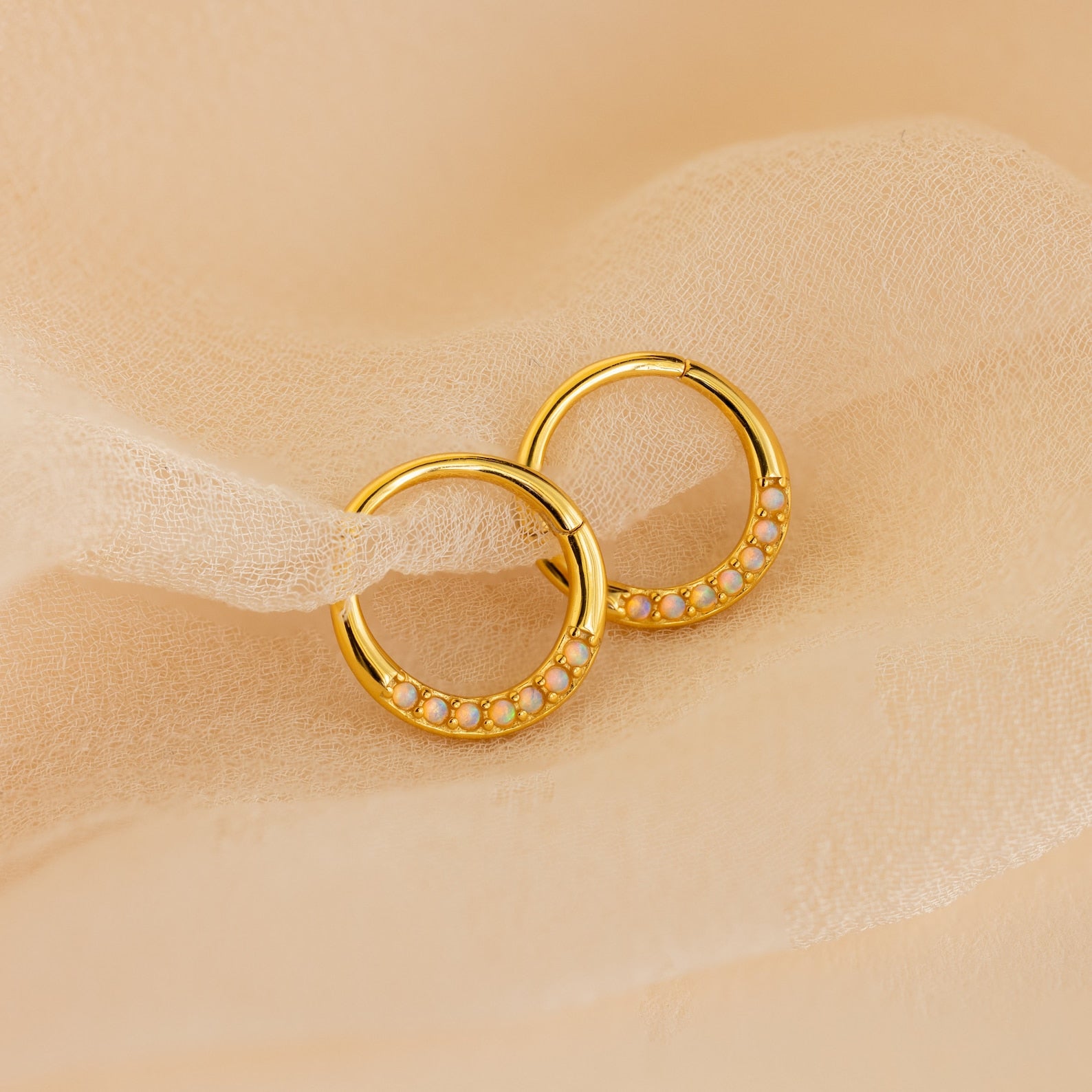 Opal Cartilage Huggies – minimalist gold hoop earrings with delicate opal gems, perfect for cartilage or everyday wear, shown on soft beige fabric.