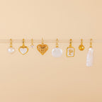 Eight gold and pearl charms, including the Round Pearl Charm in 18K Gold and a heart-shaped Mother of Pearl pendant, are displayed on a beige background.