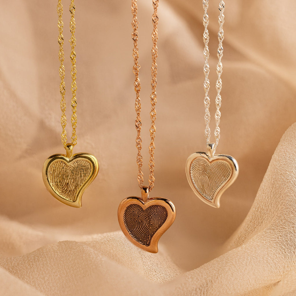 The Fingerprint Heart Necklace, available in gold, rose gold, and silver, rests on textured fabric—making a heartfelt memorial or Mother’s Day gift.