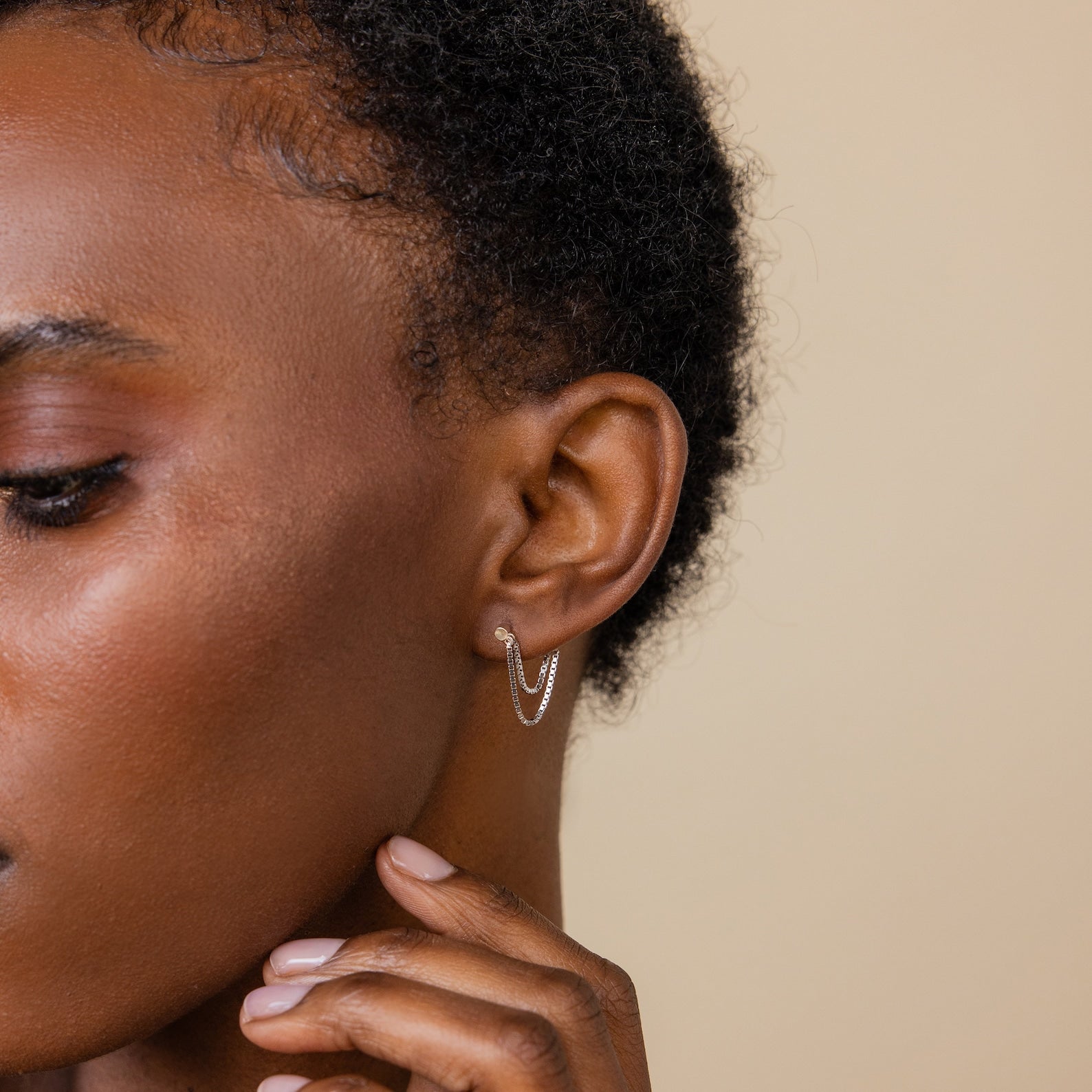 Close-up of a person gently touching their face while wearing Flatback Chain Earrings—a minimalist double hoop with a chain—perfect for creating an elegant earring stack.